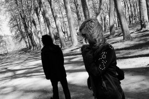 A black and white image of two individuals separated in a forest.