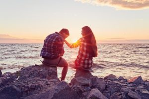 A couple sitting on rocks by the sea at sunset.