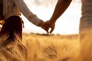 A couple holding hands in a wheat field at sunset.