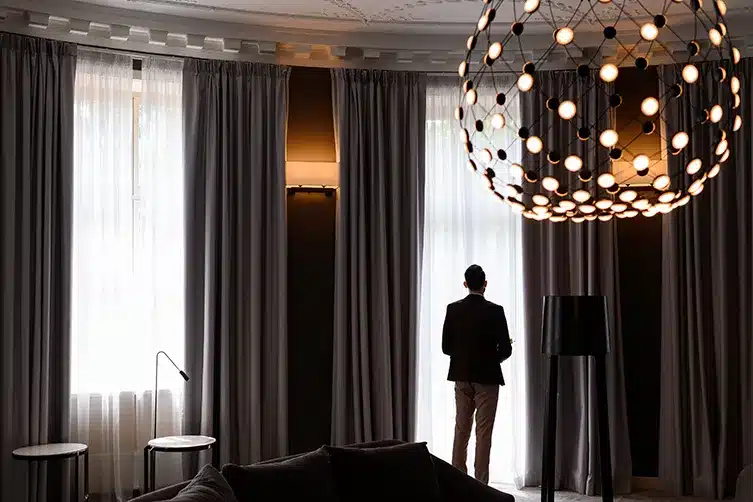 man-looking-outside-modern-room-with-gray-curtains-hanging-lamp